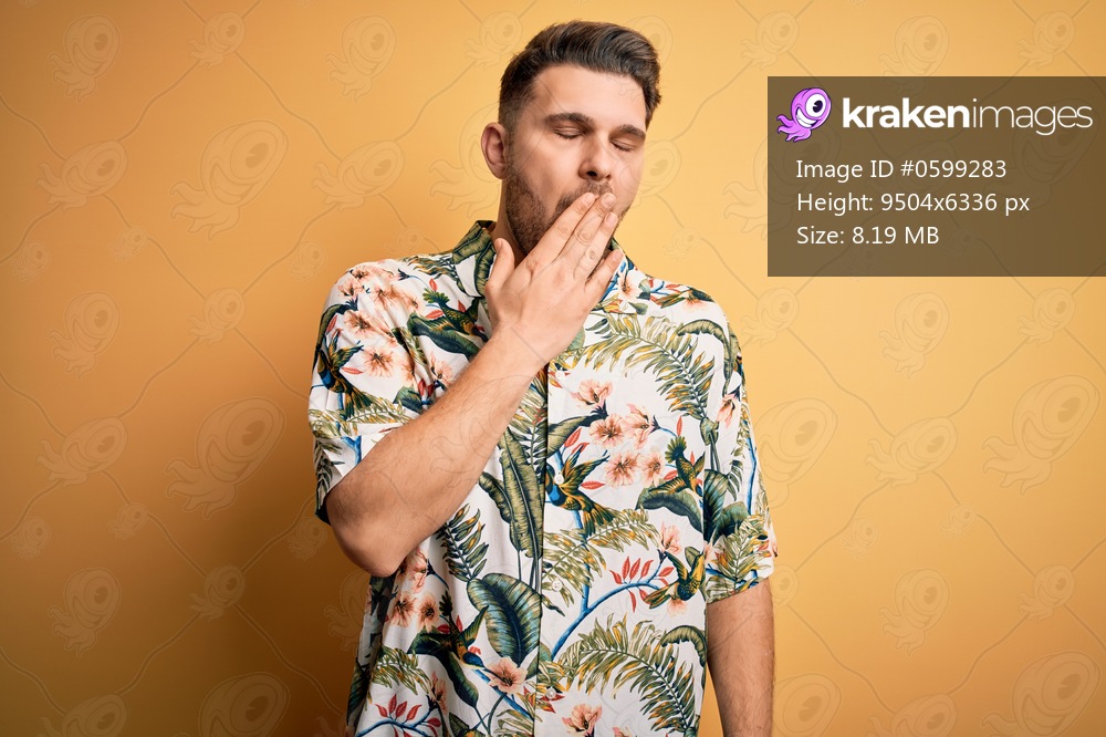 Young man with blue eyes on vacation wearing floral summer shirt over yellow background bored yawning tired covering mouth with hand. Restless and sleepiness.