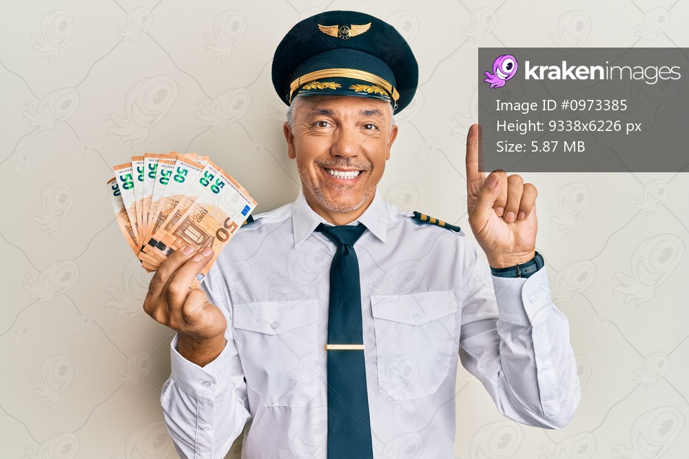 Handsome middle age mature man wearing airplane pilot uniform holding euros smiling with an idea or question pointing finger with happy face, number one 