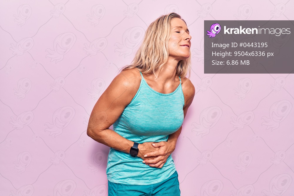 Middle age caucasian blonde woman wearing sports clothes over pink background with hand on stomach because nausea, painful disease feeling unwell. ache concept. 