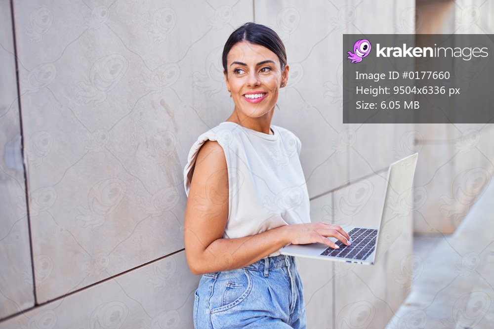 Beautiful young woman wearing fashionable clothes walking down the street and working using computer laptop