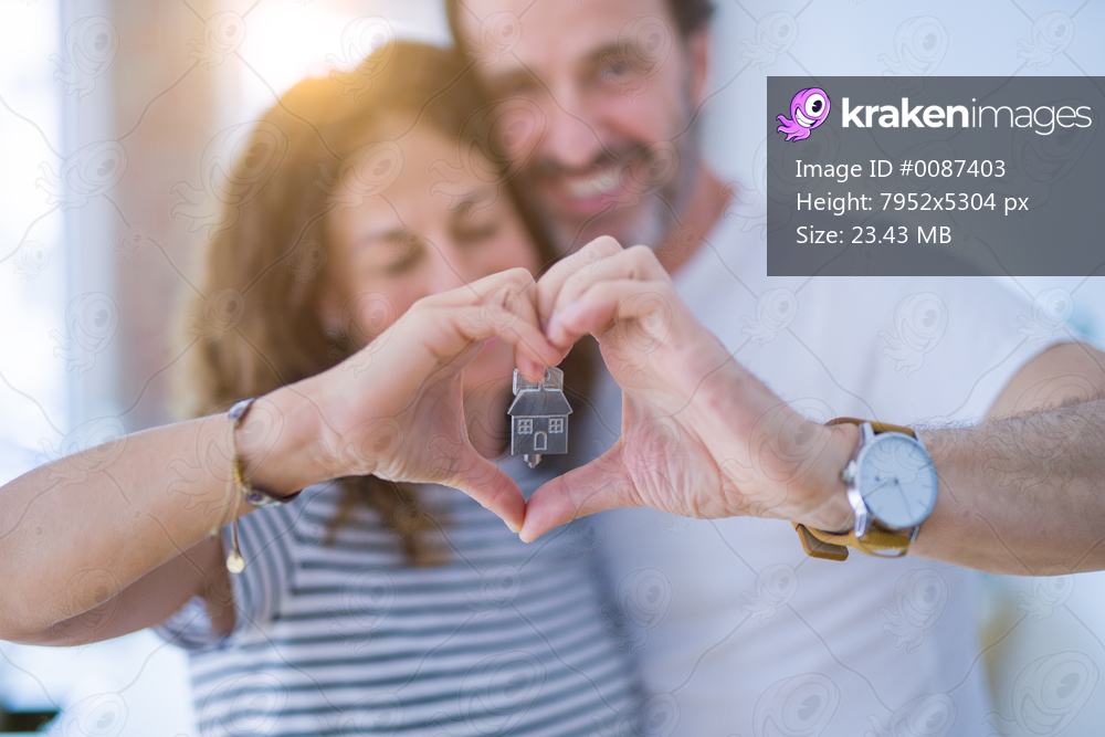Middle age senior romantic couple holding and showing house keys, doing heart shape with hands smiling happy for moving to a new home