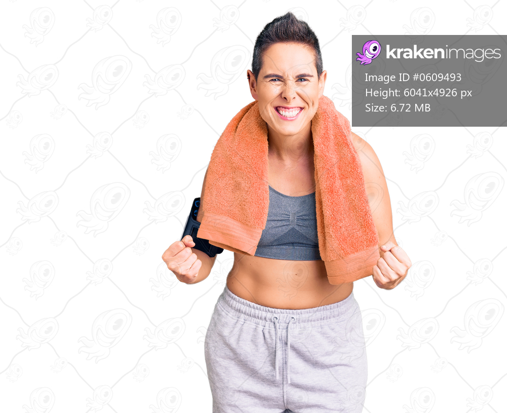Young woman with short hair wearing sportswear and towel using smartphone very happy and excited doing winner gesture with arms raised, smiling and screaming for success. celebration concept. 