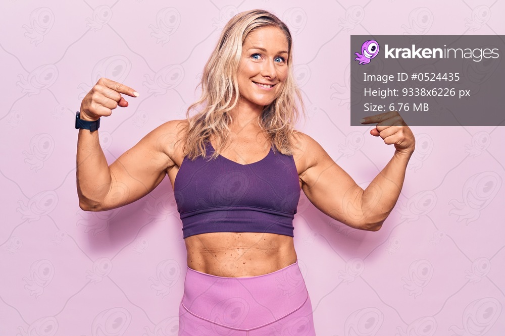 Middle age caucasian blonde woman wearing sportswear over pink background looking confident with smile on face, pointing oneself with fingers proud and happy. 