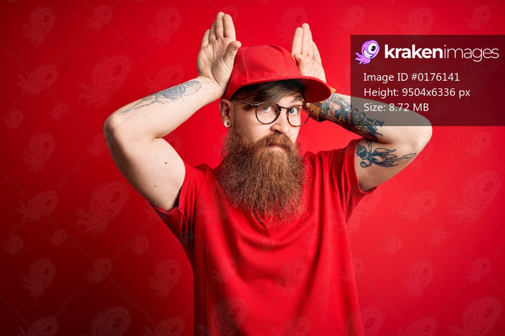 Young handsome delivery man wearing glasses and red cap over isolated background Doing bunny ears gesture with hands palms looking cynical and skeptical. Easter rabbit concept.