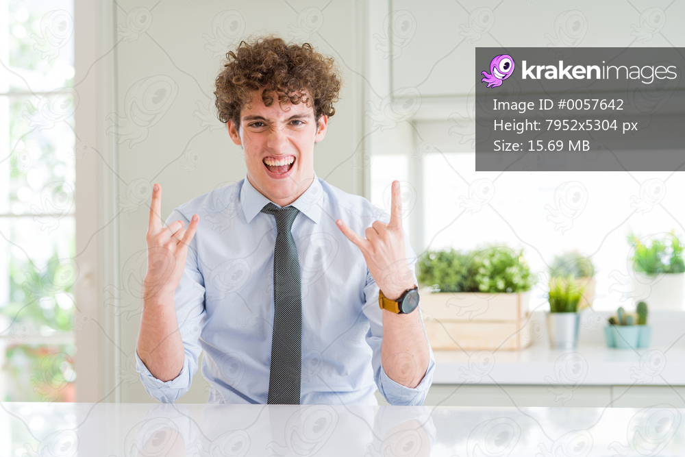 Young business man wearing a tie shouting with crazy expression doing rock symbol with hands up. Music star. Heavy concept.