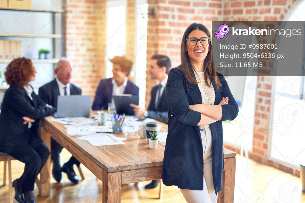 Group of business workers smiling happy and confident working together in a meeting. One of them, standing with smile on face looking at camera at the office.