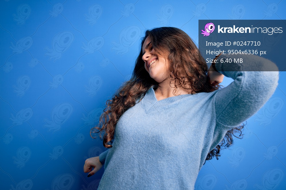 Young beautiful woman with curly hair wearing blue casual sweater over isolated background stretching back, tired and relaxed, sleepy and yawning for early morning