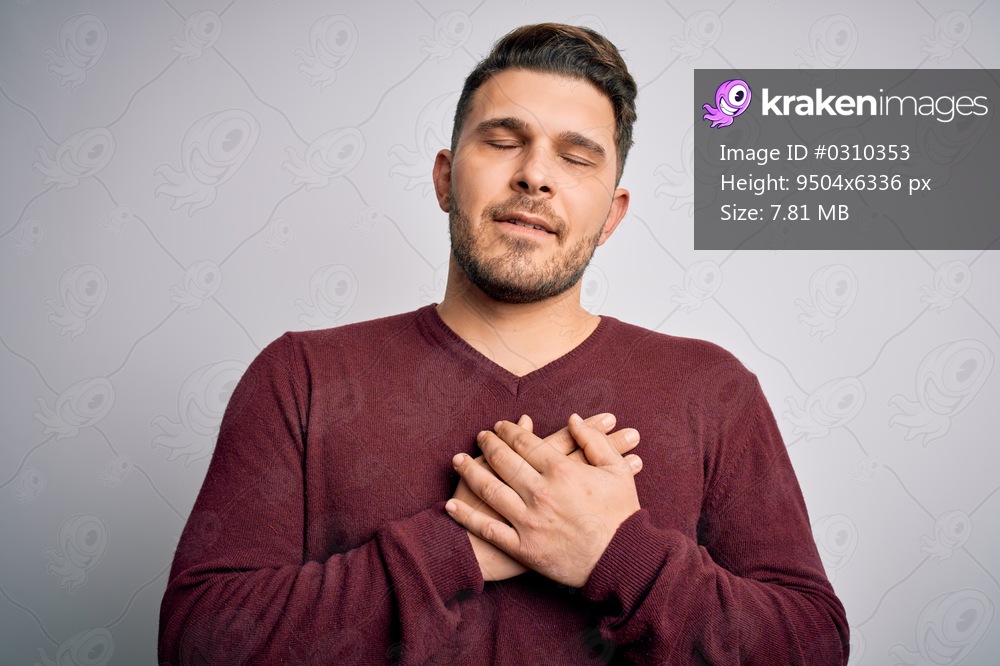 Young man with blue eyes wearing casual sweater standing over isolated background smiling with hands on chest with closed eyes and grateful gesture on face. Health concept.