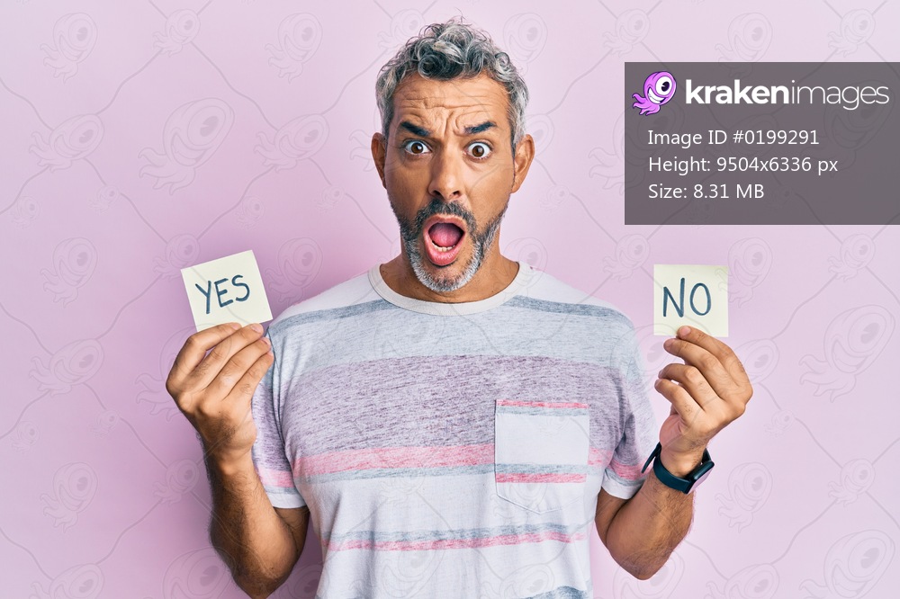 Middle age grey-haired man holding yes and no reminder afraid and shocked with surprise and amazed expression, fear and excited face. 