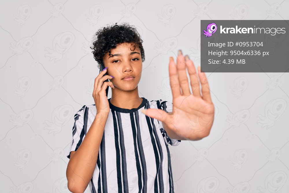 Young beautiful african american afro woman having conversation talking on the smartphone with open hand doing stop sign with serious and confident expression, defense gesture