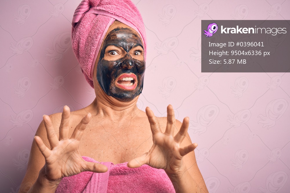 Middle age brunette woman wearing beauty black face mask over isolated pink background afraid and terrified with fear expression stop gesture with hands, shouting in shock. Panic concept.