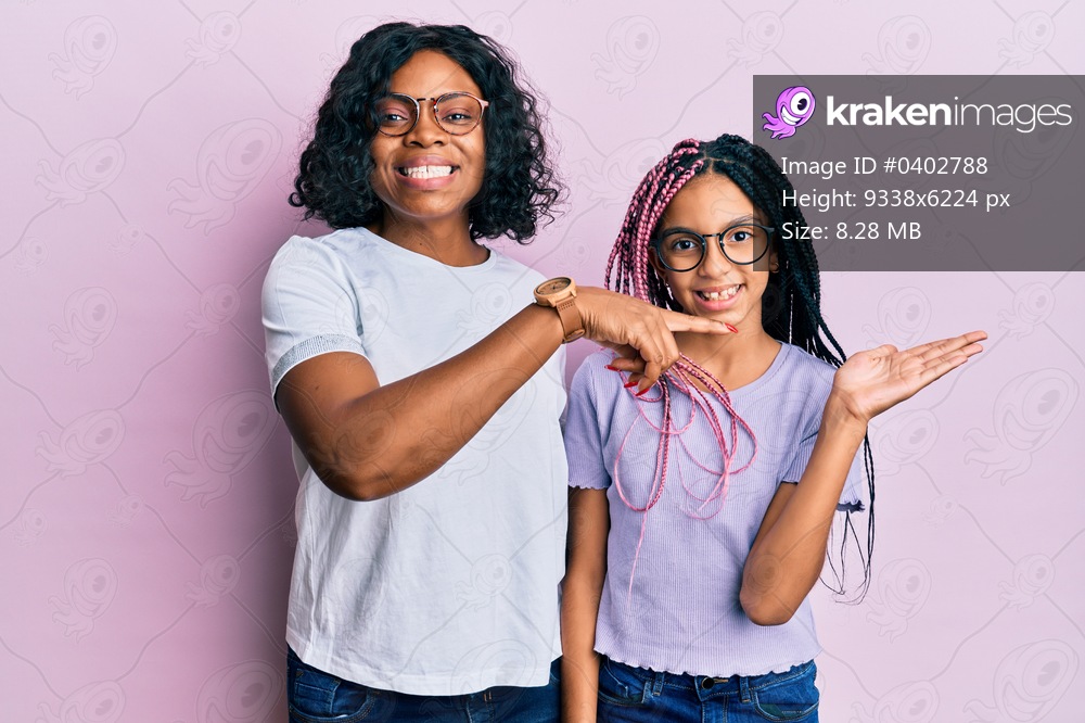 Beautiful african american mother and daughter wearing casual clothes and glasses amazed and smiling to the camera while presenting with hand and pointing with finger. 