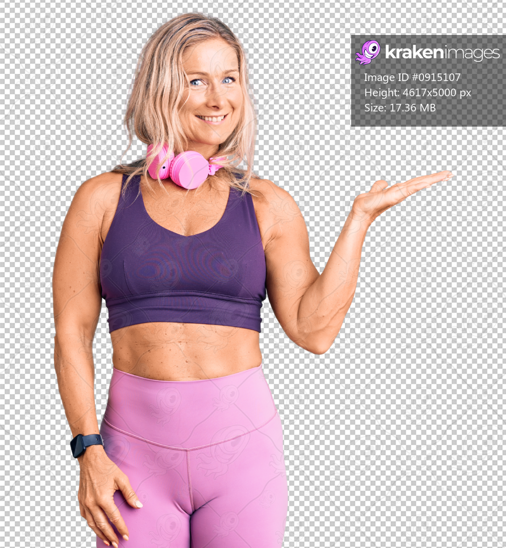 Middle age fit blonde woman wearing gym clothes and using headphones smiling cheerful presenting and pointing with palm of hand looking at the camera.