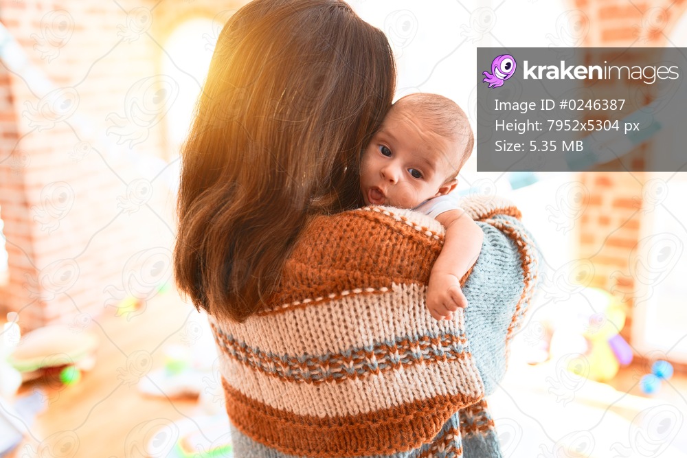 Young beautiful woman and her baby standing at home. Mother holding and hugging newborn