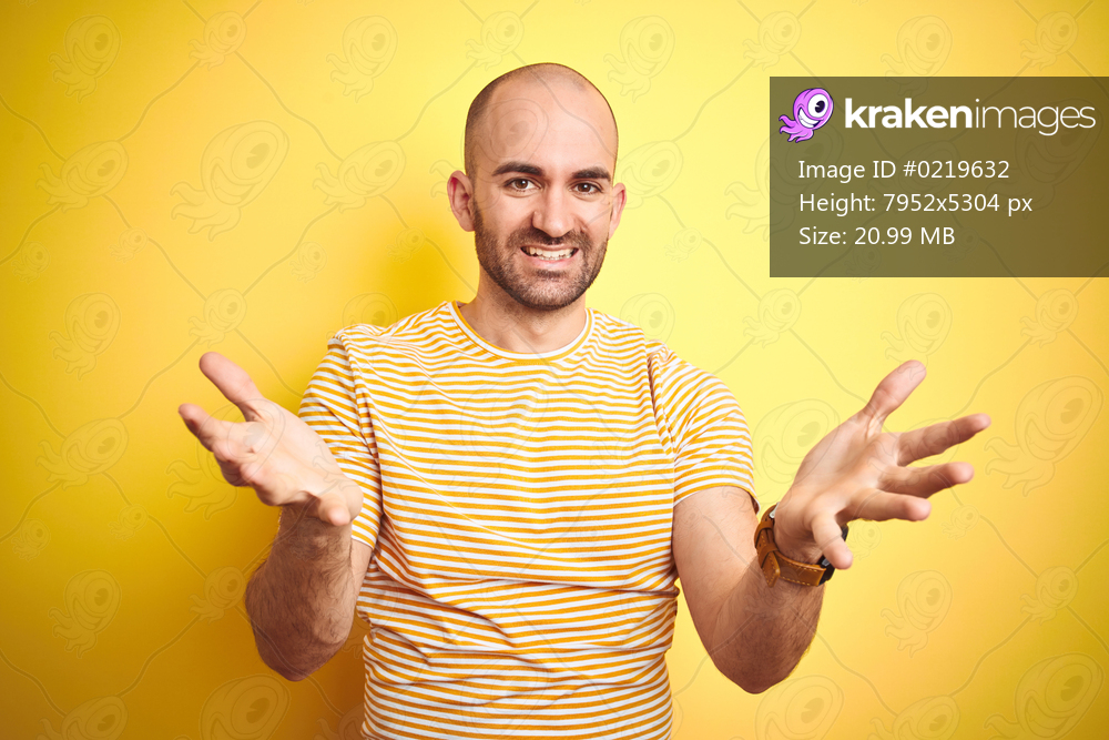 Young bald man with beard wearing casual striped t-shirt over yellow isolated background smiling cheerful offering hands giving assistance and acceptance.