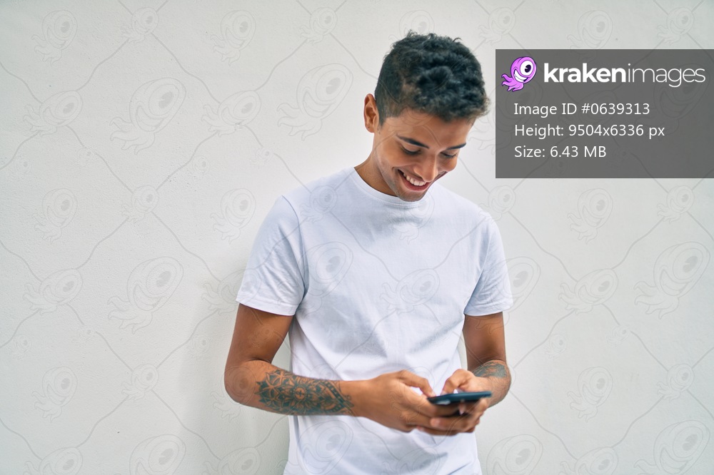 Young latin man smiling happy using smartphone walking at the city.