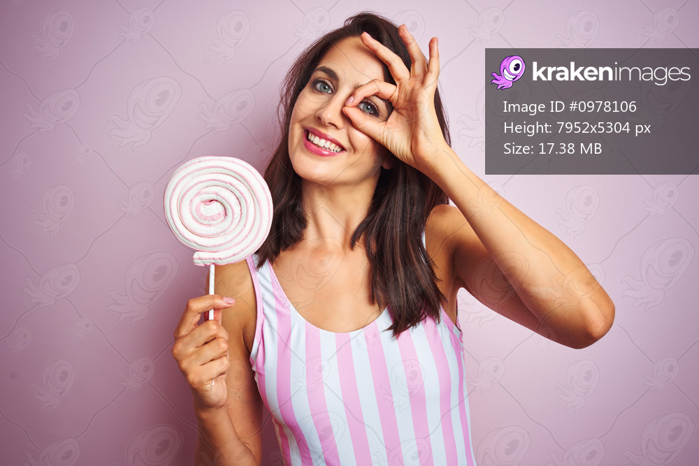 Young beautiful woman eating sweet candy over pink isolated background with happy face smiling doing ok sign with hand on eye looking through fingers