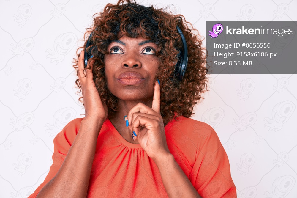 Young african american woman listening to music using headphones serious face thinking about question with hand on chin, thoughtful about confusing idea 