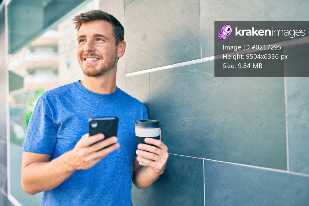 Young caucasian man using smartphone and drinking take away coffee at the city.