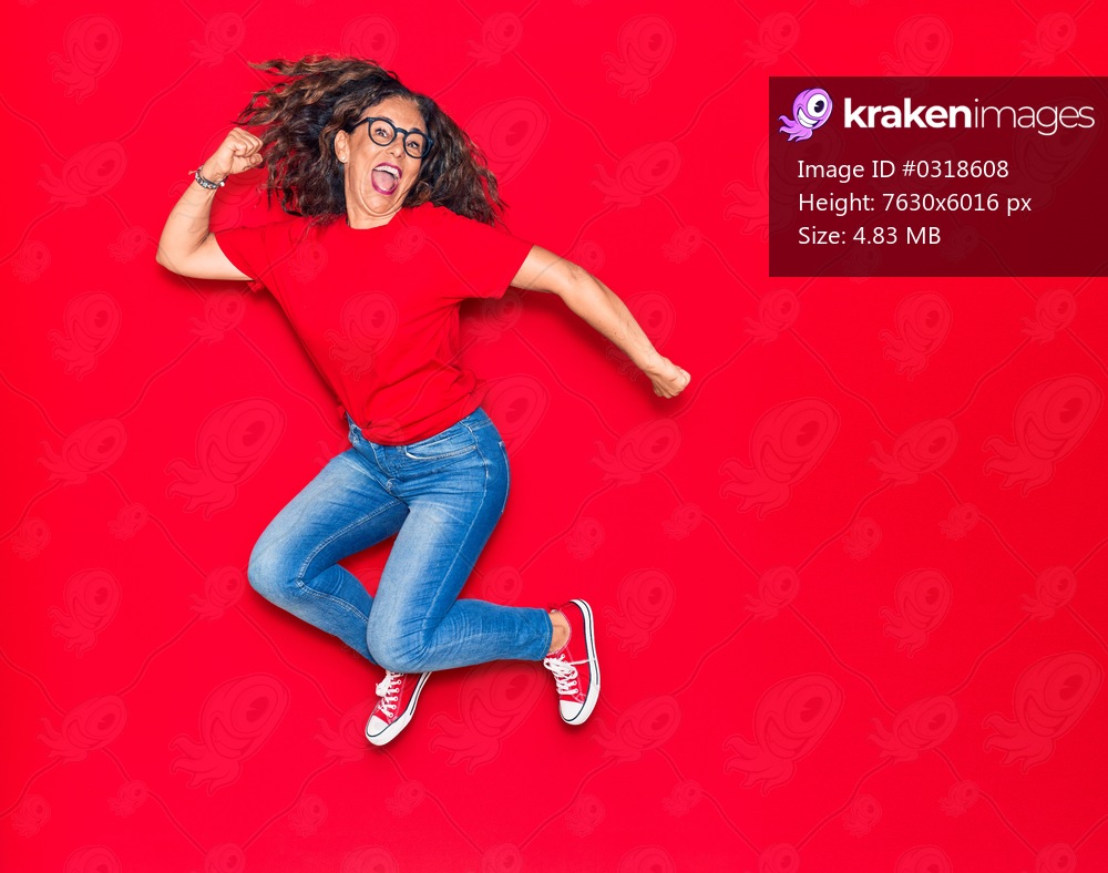 Middle age beautiful hispanic woman wearing casual clothes and glasses smiling happy. Jumping with smile on face over isolated red background