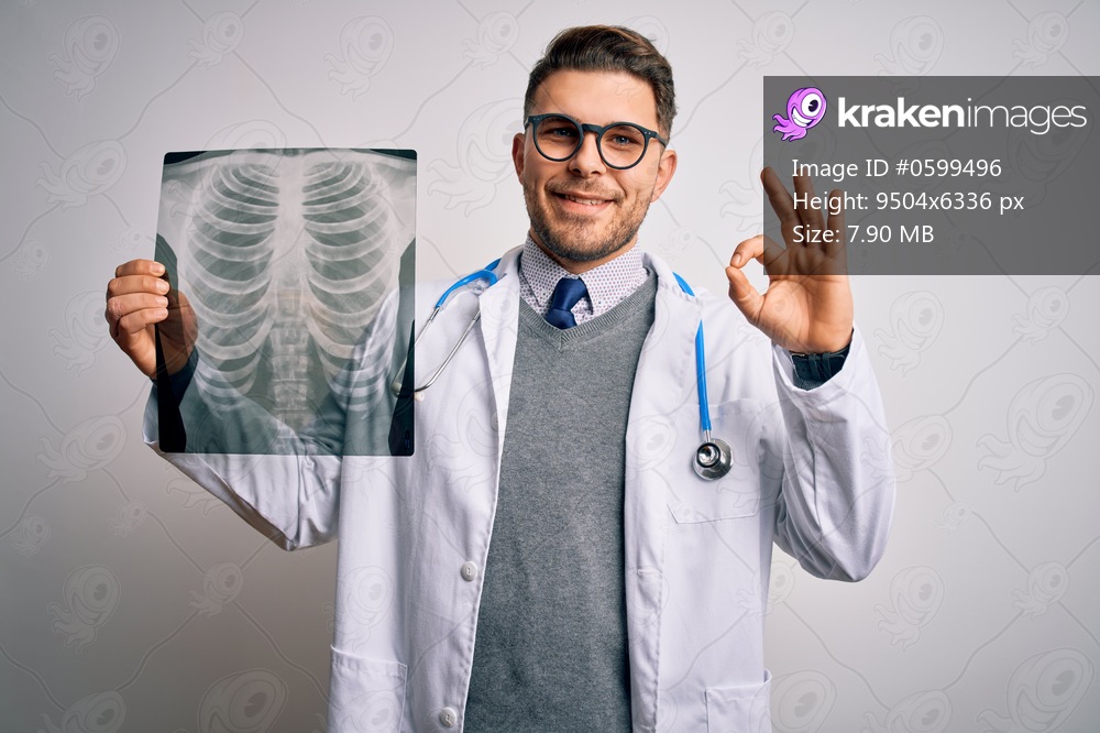 Young doctor man wearing medical coat looking at chest scan radiography over isolated background doing ok sign with fingers, excellent symbol