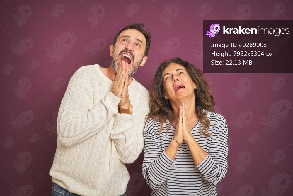 Beautiful middle age couple wearing winter sweater over isolated purple background begging and praying with hands together with hope expression on face very emotional and worried. Asking for forgiveness. Religion concept.