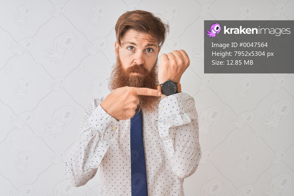 Young redhead irish businessman standing over isolated white background In hurry pointing to watch time, impatience, looking at the camera with relaxed expression