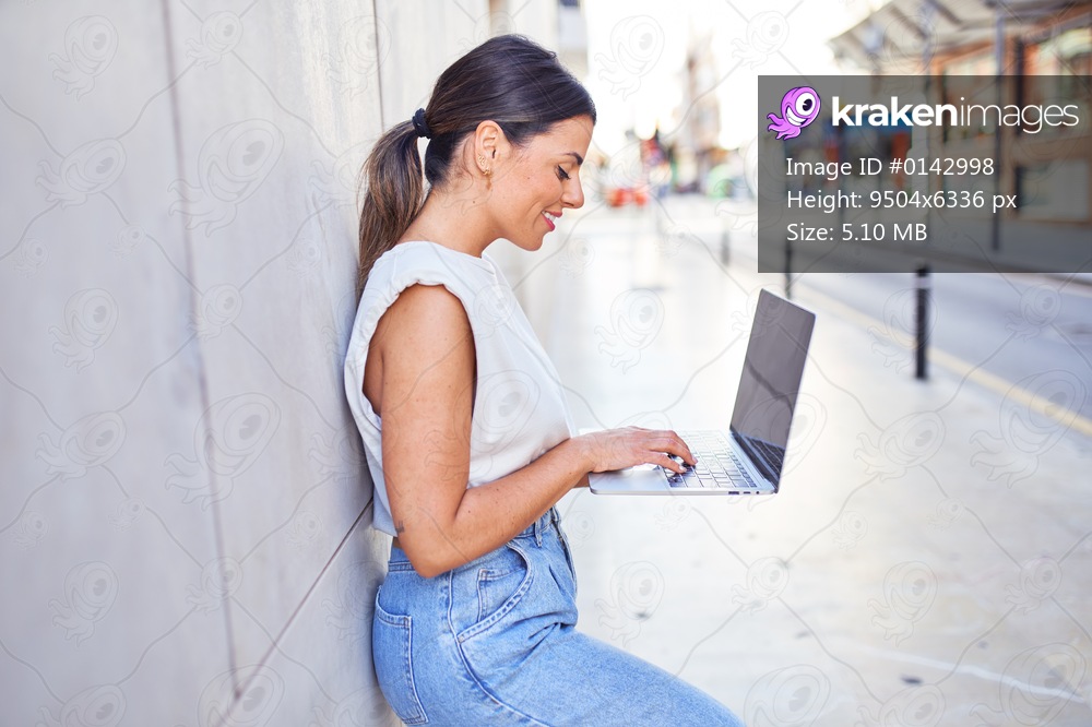 Beautiful young woman wearing fashionable clothes walking down the street and working using computer laptop