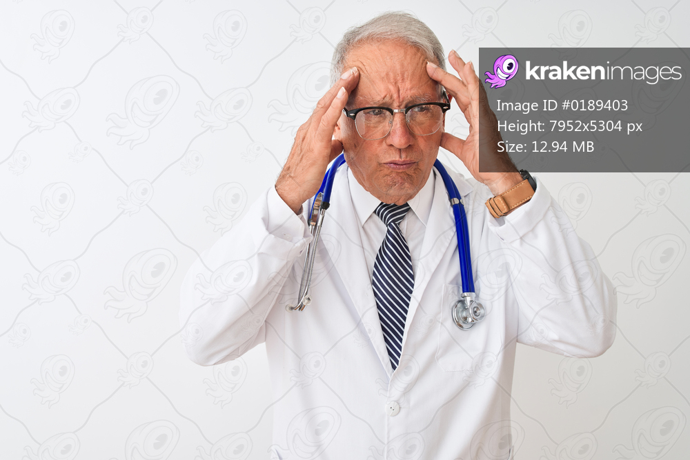 Senior grey-haired doctor man wearing stethoscope standing over isolated white background with hand on head for pain in head because stress. Suffering migraine.