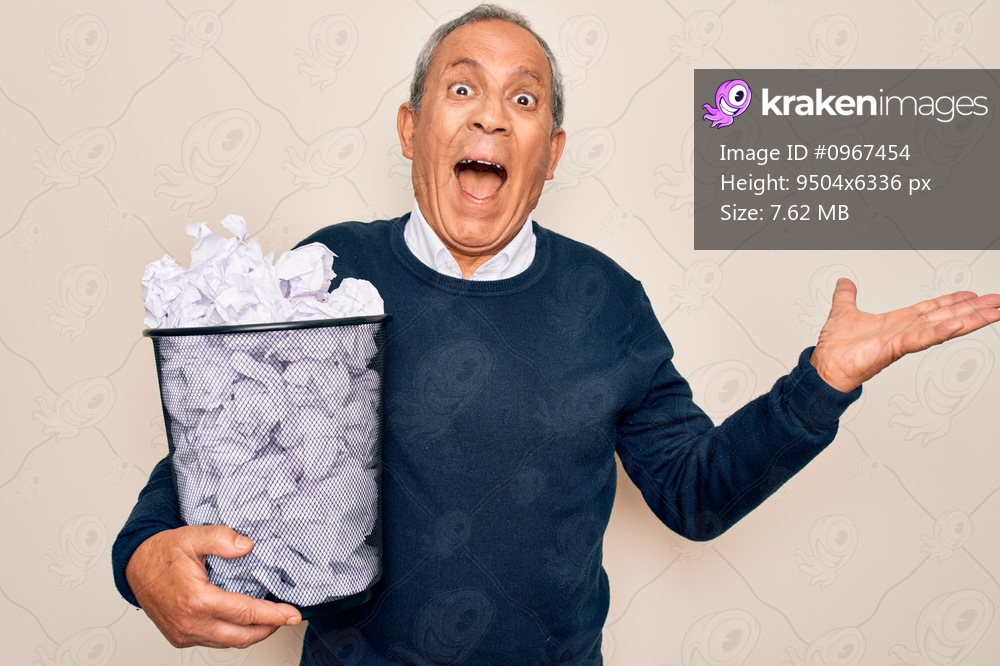 Senior grey-haired man holding full paper bin with crumpled papers over white background very happy and excited, winner expression celebrating victory screaming with big smile and raised hands