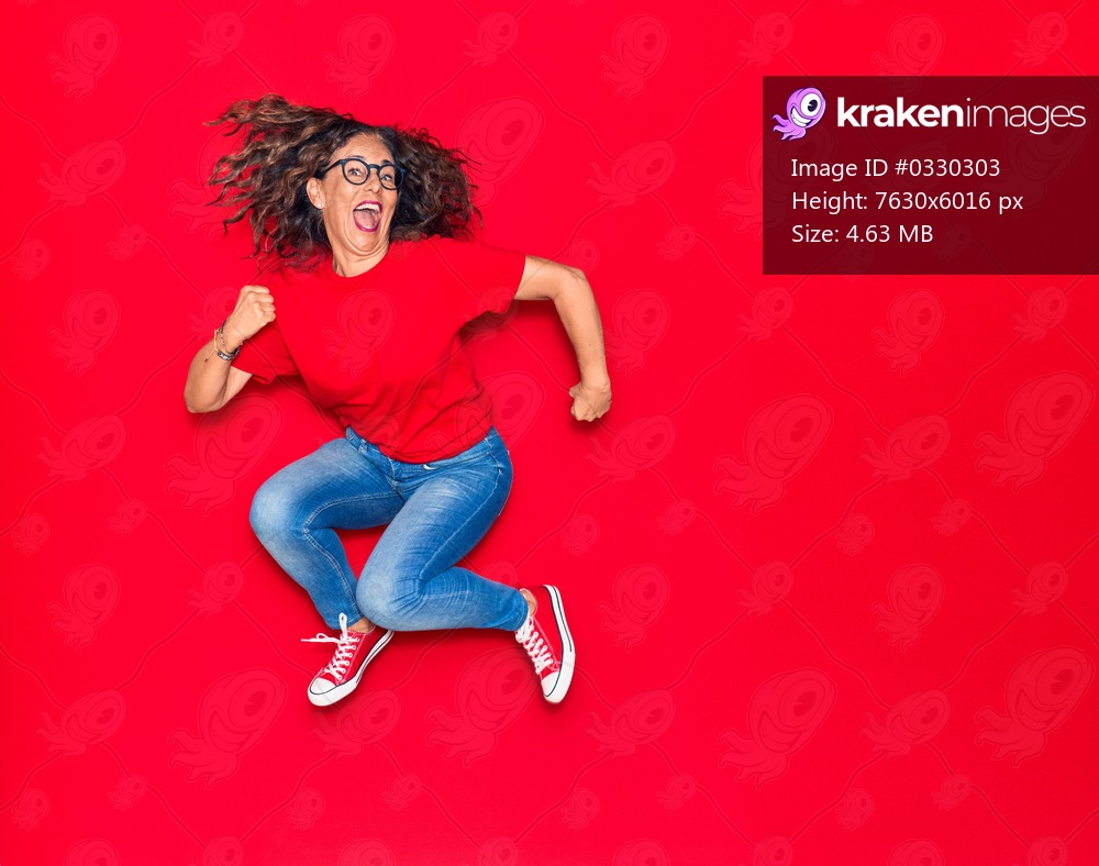 Middle age beautiful hispanic woman wearing casual clothes and glasses smiling happy. Jumping with smile on face over isolated red background