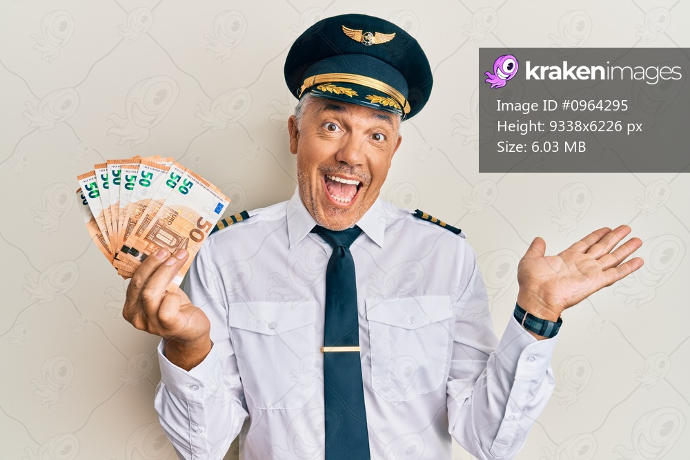 Handsome middle age mature man wearing airplane pilot uniform holding euros celebrating achievement with happy smile and winner expression with raised hand 