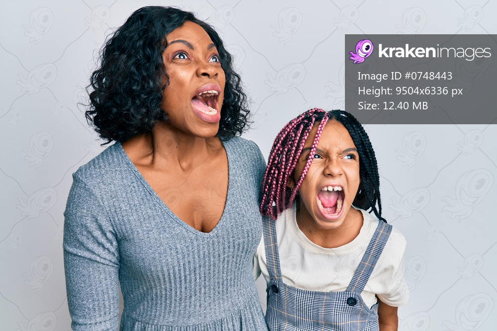 Beautiful african american mother and daughter wearing casual clothes and hugging angry and mad screaming frustrated and furious, shouting with anger. rage and aggressive concept. 