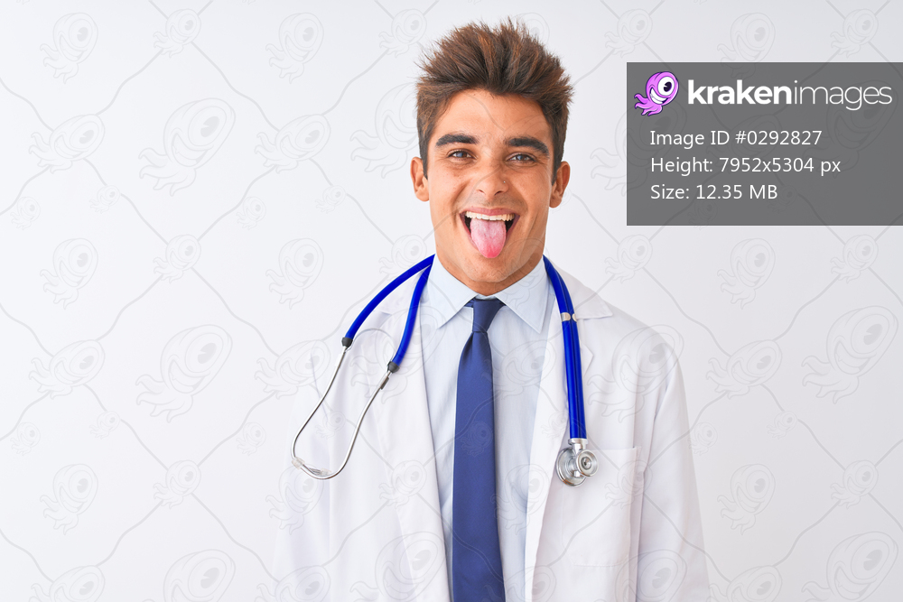 Young handsome doctor man wearing stethoscope over isolated white background sticking tongue out happy with funny expression. Emotion concept.