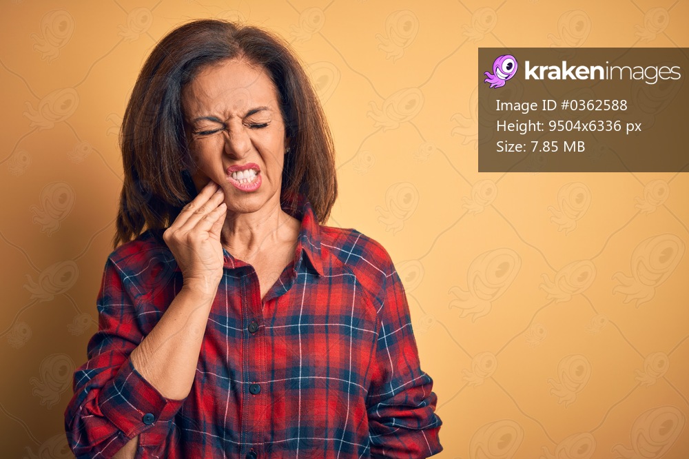 Middle age beautiful woman wearing casual shirt standing over isolated yellow background touching mouth with hand with painful expression because of toothache or dental illness on teeth. Dentist