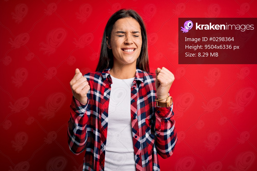 Young beautiful brunette woman wearing casual shirt standing over isolated red background excited for success with arms raised and eyes closed celebrating victory smiling. Winner concept.