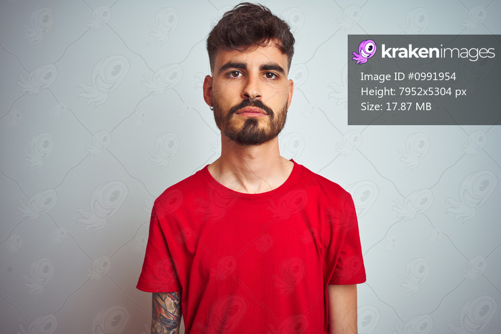 Young man with tattoo wearing red t-shirt standing over isolated white background Relaxed with serious expression on face. Simple and natural looking at the camera.