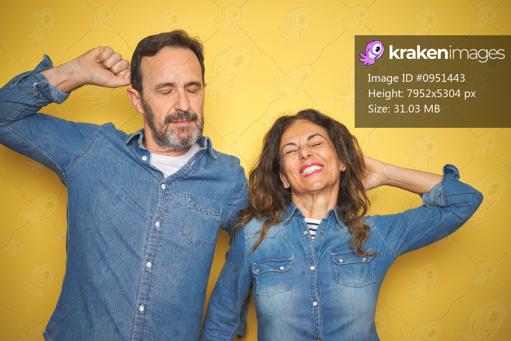 Beautiful middle age couple together standing over isolated yellow background stretching back, tired and relaxed, sleepy and yawning for early morning