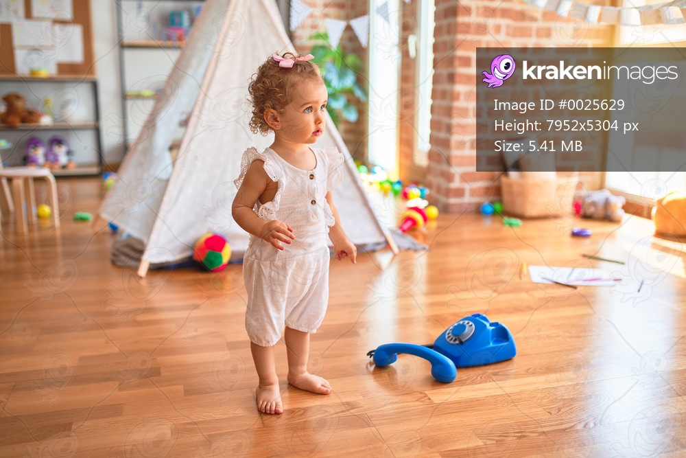 Beautiful caucasian infant playing with toys at colorful playroom. Happy and playful calling with vitange telephone at kindergarten.