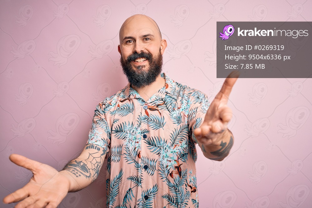 Handsome bald man with beard and tattoo wearing casual floral shirt over pink background smiling cheerful offering hands giving assistance and acceptance.