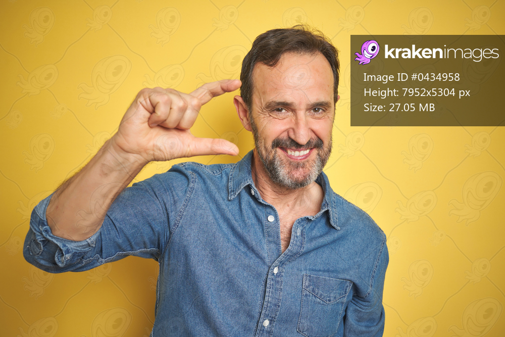 Handsome middle age senior man with grey hair over isolated yellow background smiling and confident gesturing with hand doing small size sign with fingers looking and the camera. Measure concept.