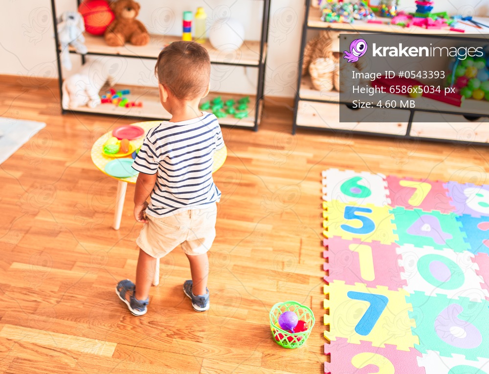 Beautiful toddler boy playing meals with plastic plates, fruits and vegetables at kindergarten