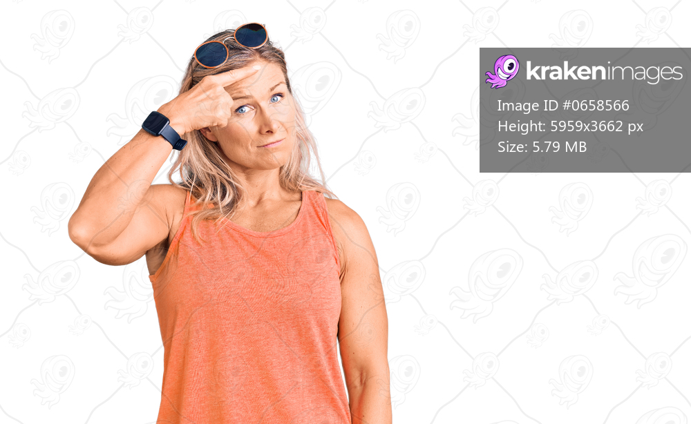 Middle age fit blonde woman wearing casual summer clothes and sunglasses pointing unhappy to pimple on forehead, ugly infection of blackhead. acne and skin problem 