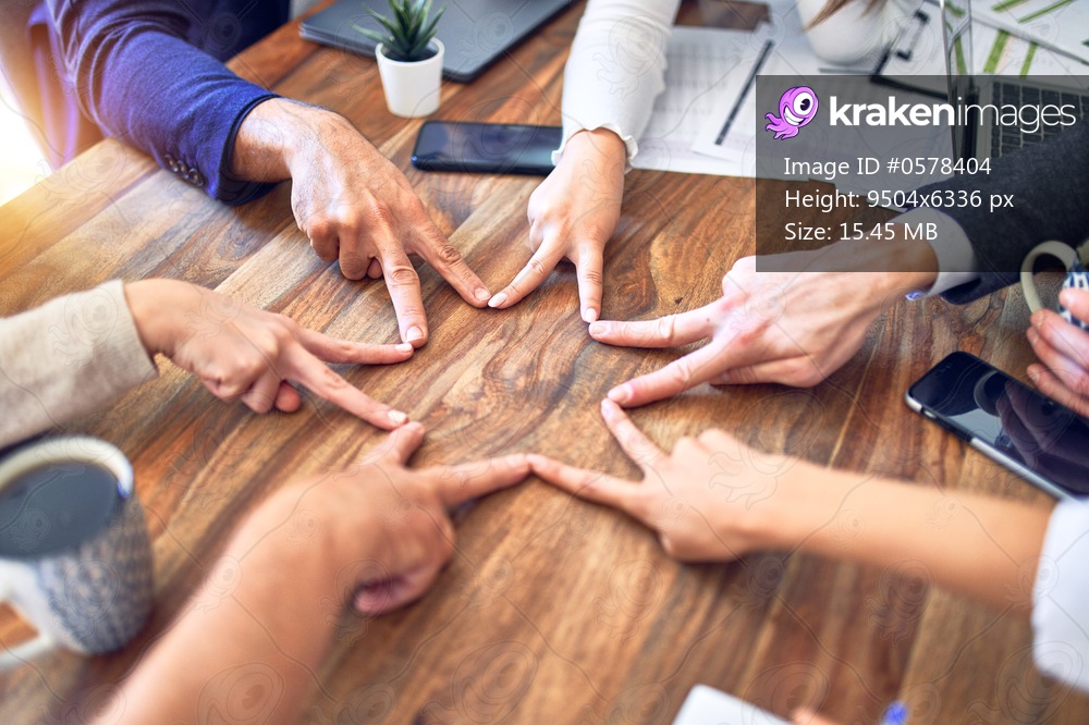 Group of business workers standing with hands together. Doing symbol with fingers at the office