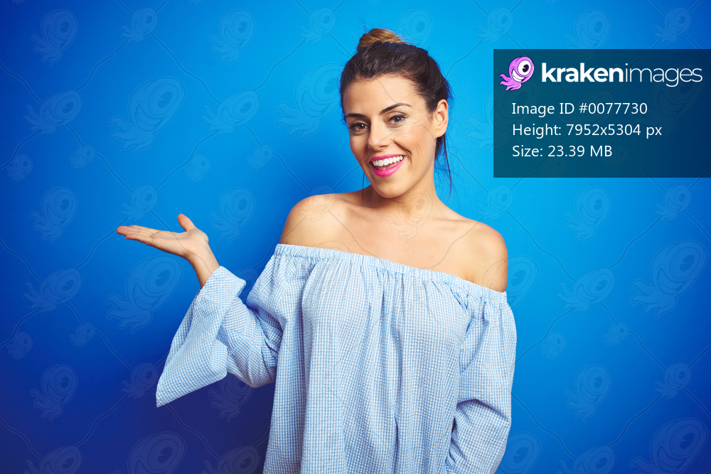 Young beautiful woman wearing bun hairstyle over blue isolated background smiling cheerful presenting and pointing with palm of hand looking at the camera.