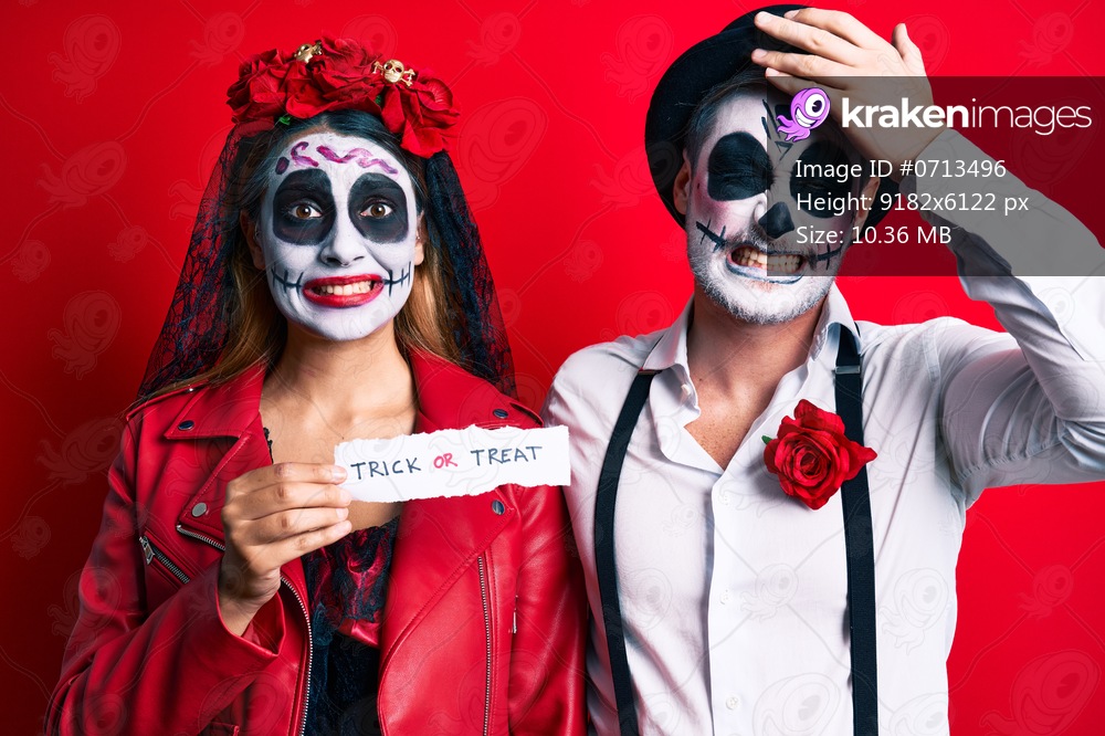 Couple wearing day of the dead costume holding trick or treat paper stressed and frustrated with hand on head, surprised and angry face 