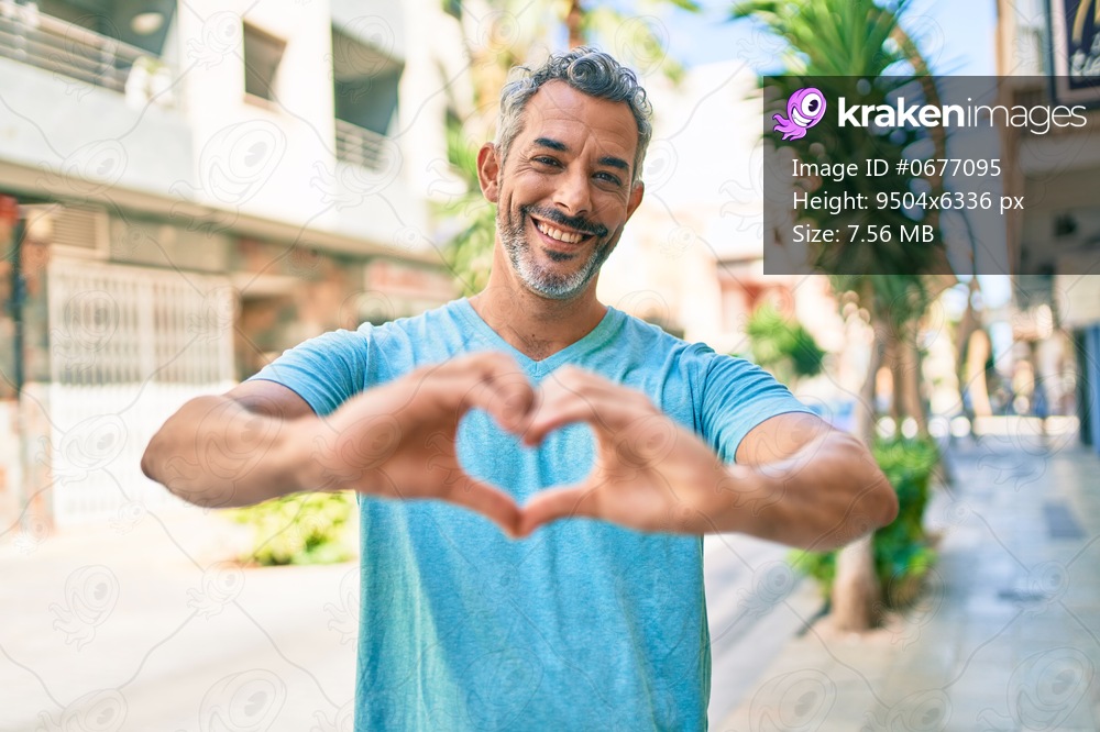 Middle age grey-haired man wearing casual clothes at street of city smiling in love showing heart symbol and shape with hands. romantic concept. 