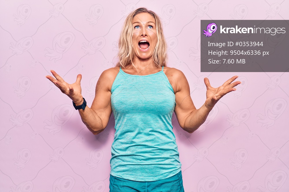 Middle age caucasian blonde woman wearing sports clothes over pink background crazy and mad shouting and yelling with aggressive expression and arms raised. frustration concept. 