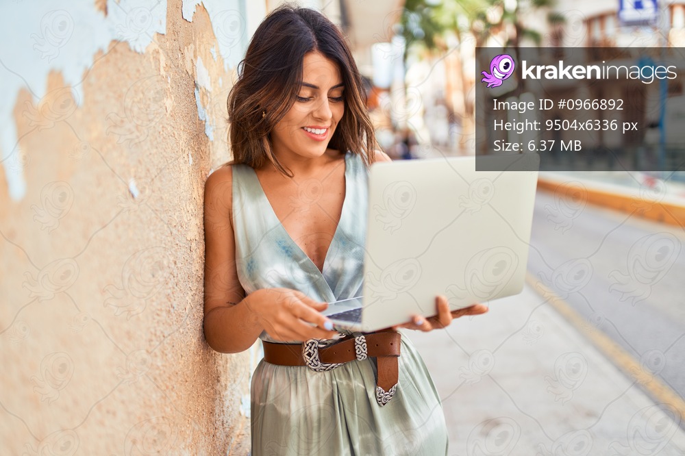 Beautiful young woman wearing fashionable clothes walking down the street and working using computer laptop
