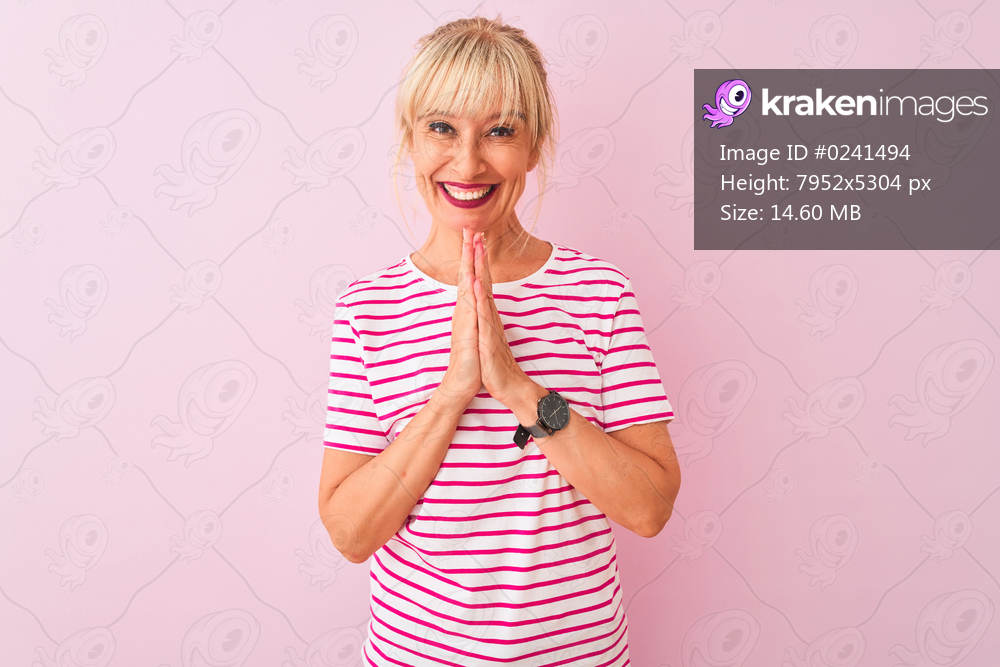 Middle age woman wearing striped t-shirt standing over isolated pink background praying with hands together asking for forgiveness smiling confident.